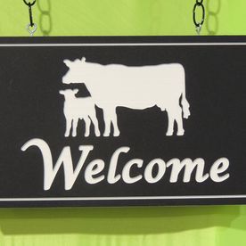 Black welcome sign with white cow and calf silhouettes.