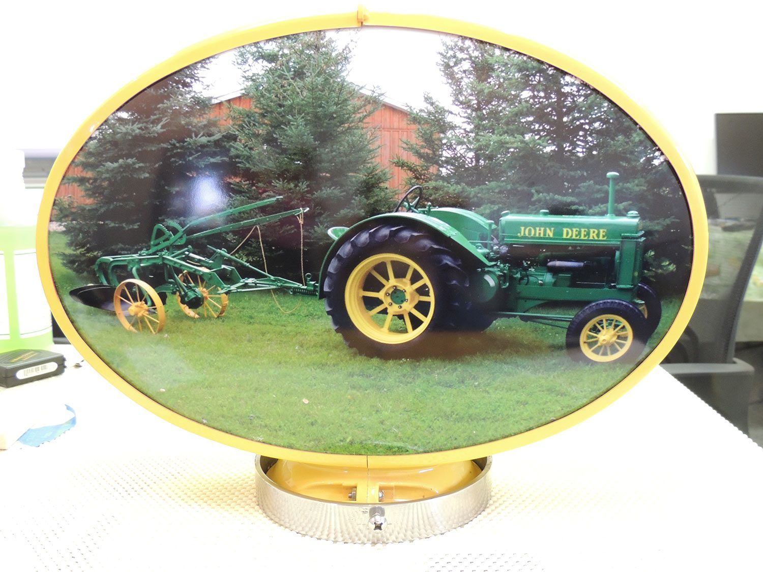 Oval sign with green and yellow New Deal tractor towing a plow, trees and building background.