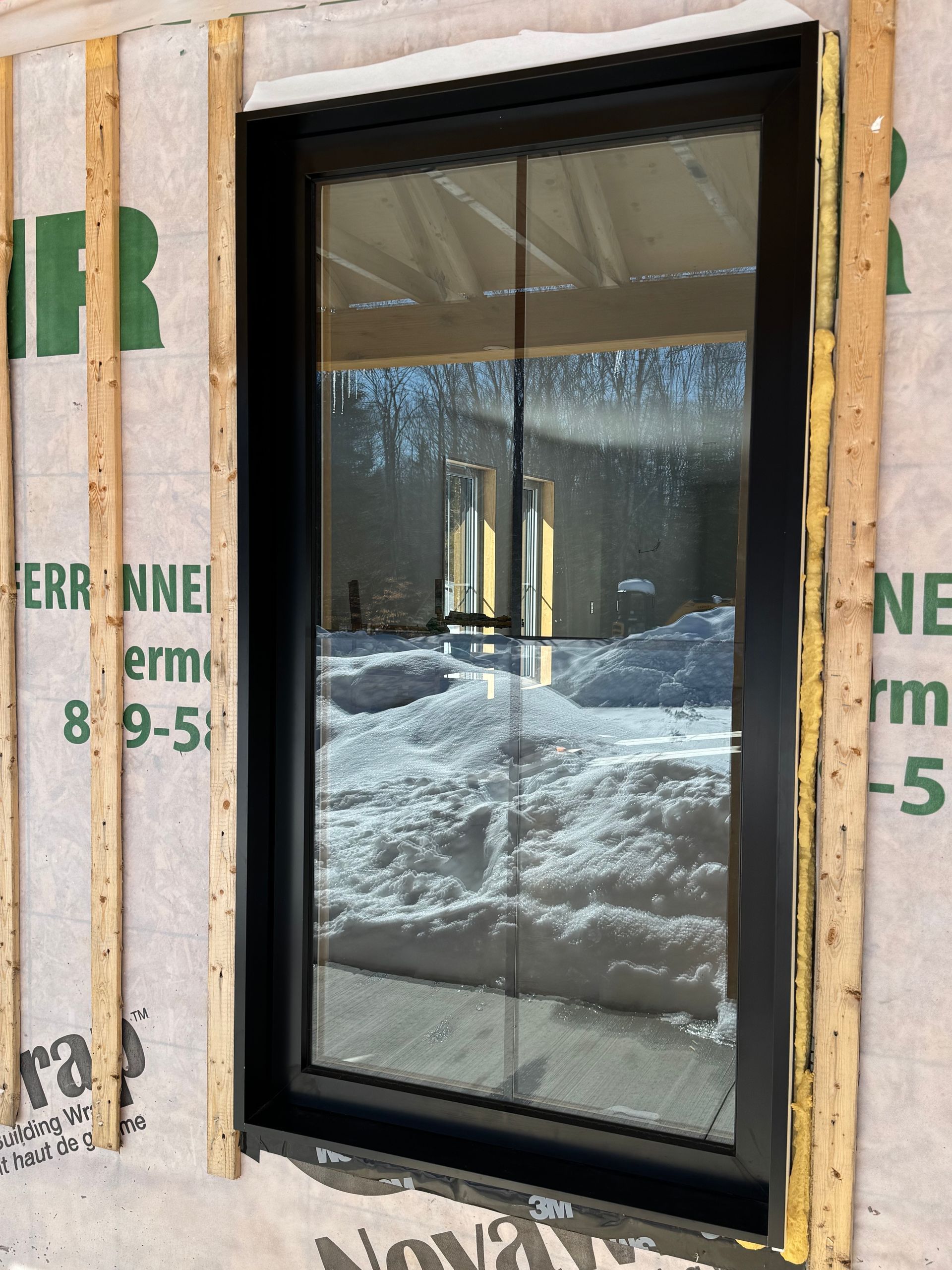 Une fenêtre à cadre noir nouvellement installée sur la façade d'un bâtiment à ossature bois et pare-vapeur résistant aux intempéries.