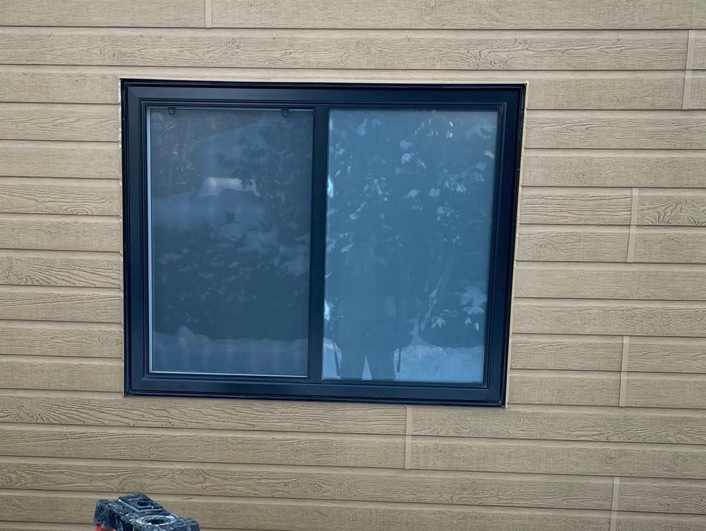 Une fenêtre coulissante à cadre noir installée dans un mur extérieur horizontal en bardage texturé beige.