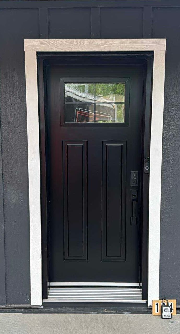 Une porte d'entrée noire avec une fenêtre encadrée de pierre blanche, sur fond de façade gris foncé.