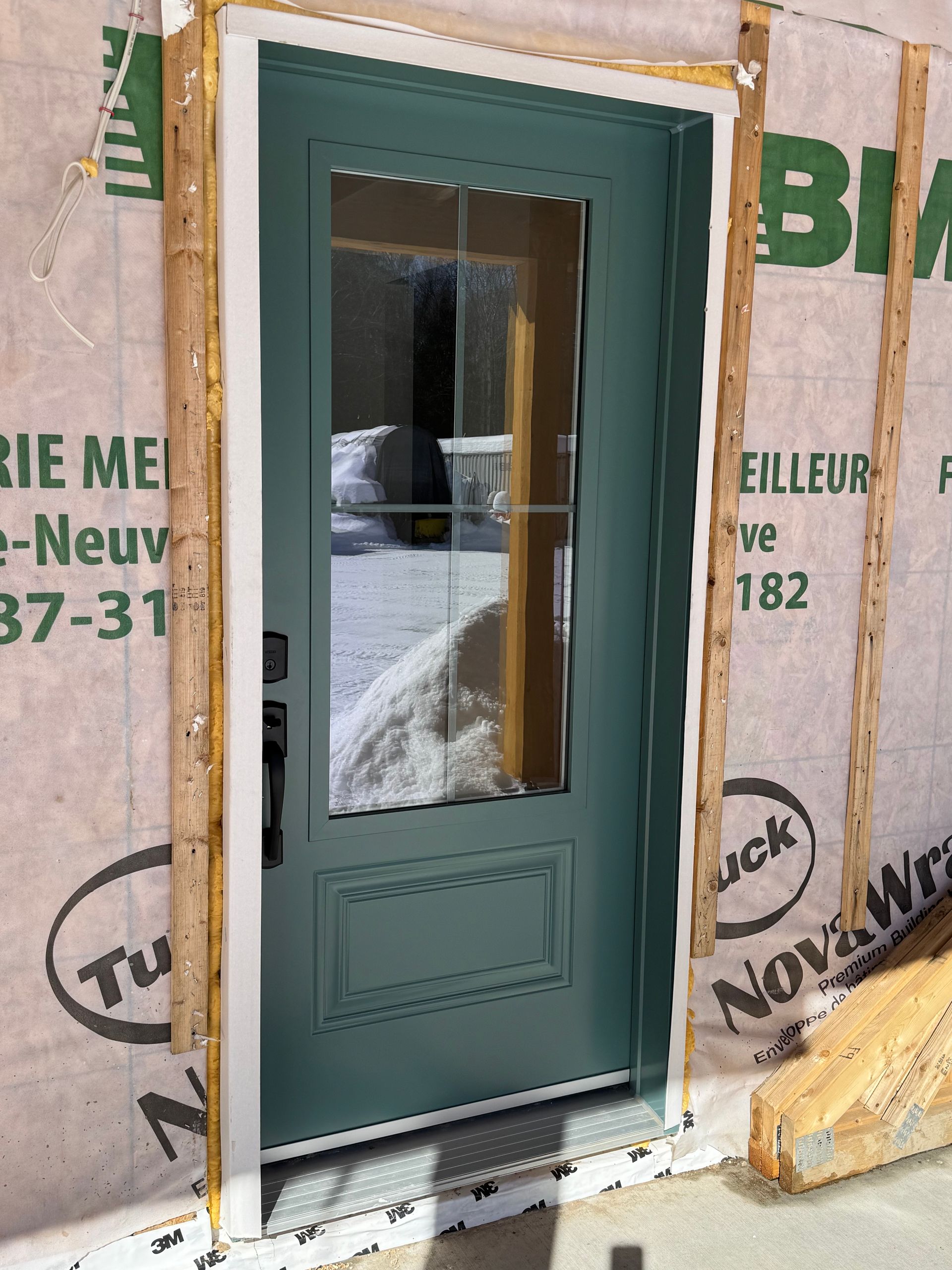 Une porte extérieure verte avec une fenêtre, installée dans un mur de chantier recouvert d'un pare-vapeur NovaWrap.