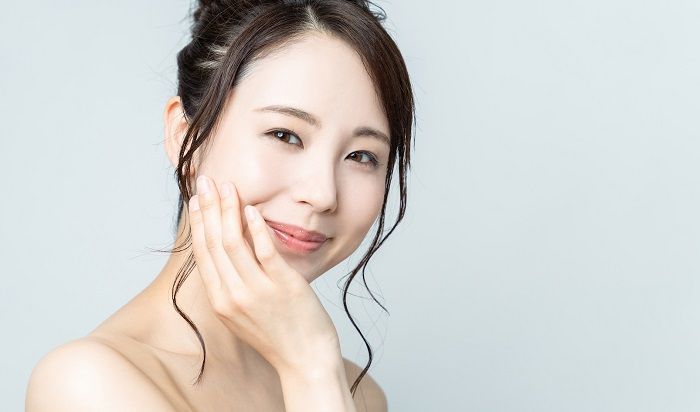 A woman is touching her face with her hand and smiling.