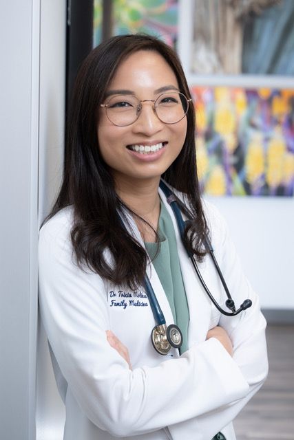 Dr. Tricia Molina, a concierge doctor, in a white lab coat is wearing a stethoscope and smiling