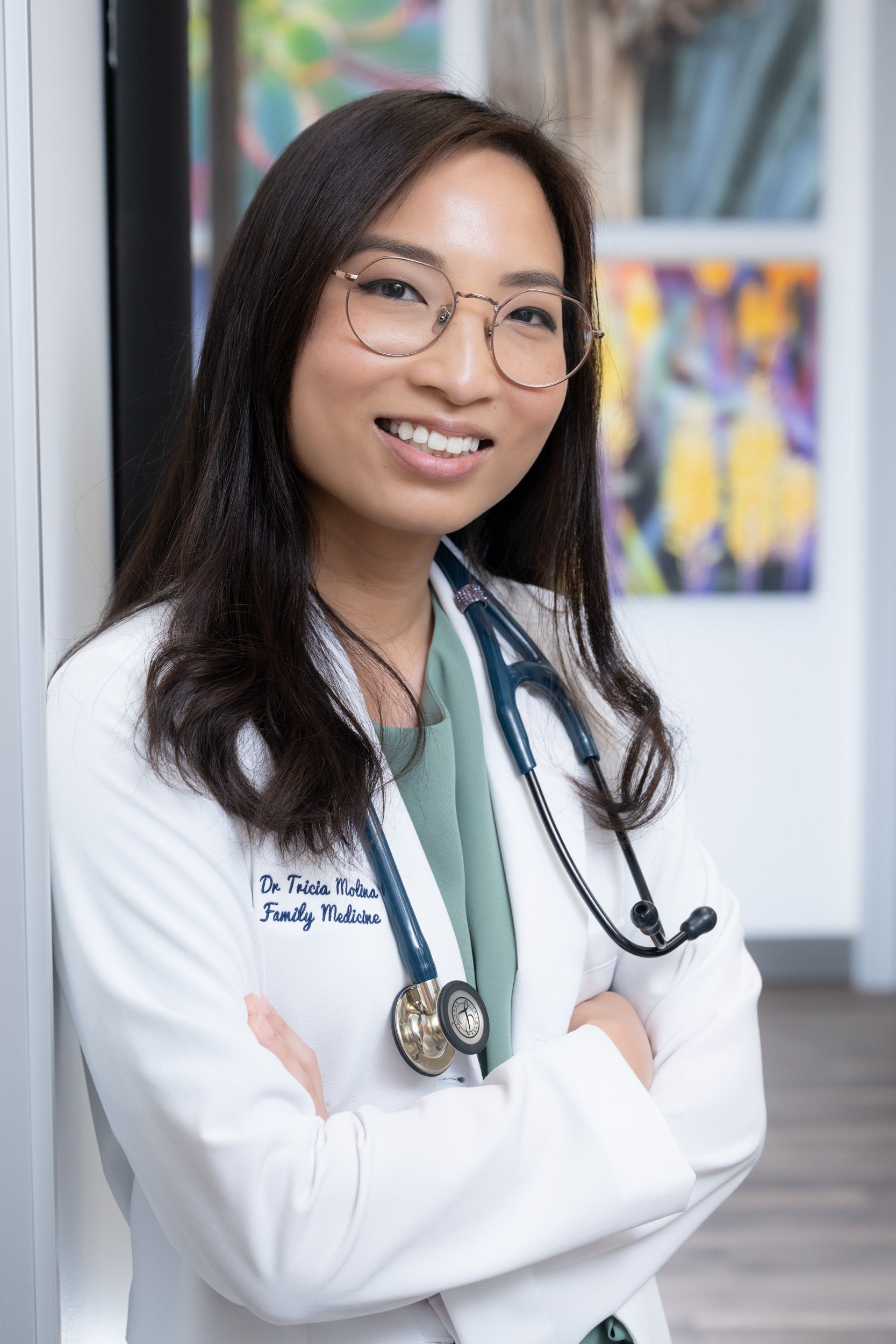 A young woman in a white lab coat is holding a stethoscope and smiling