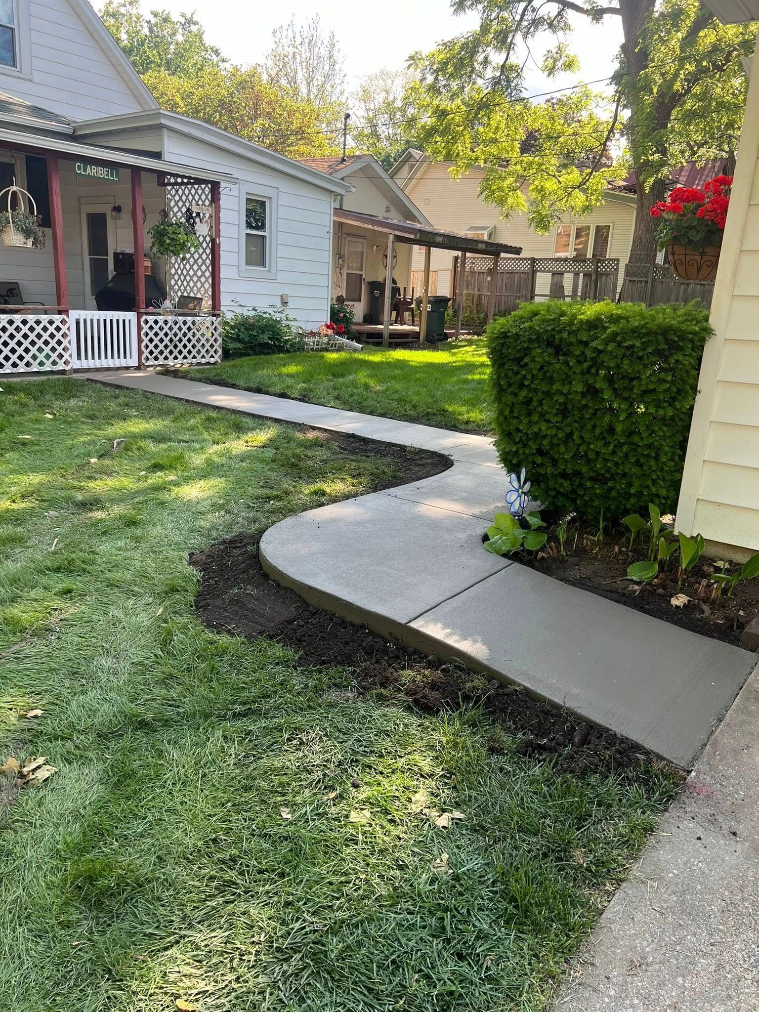 Concrete sidewalk curves through a green yard in front of houses on a sunny day.