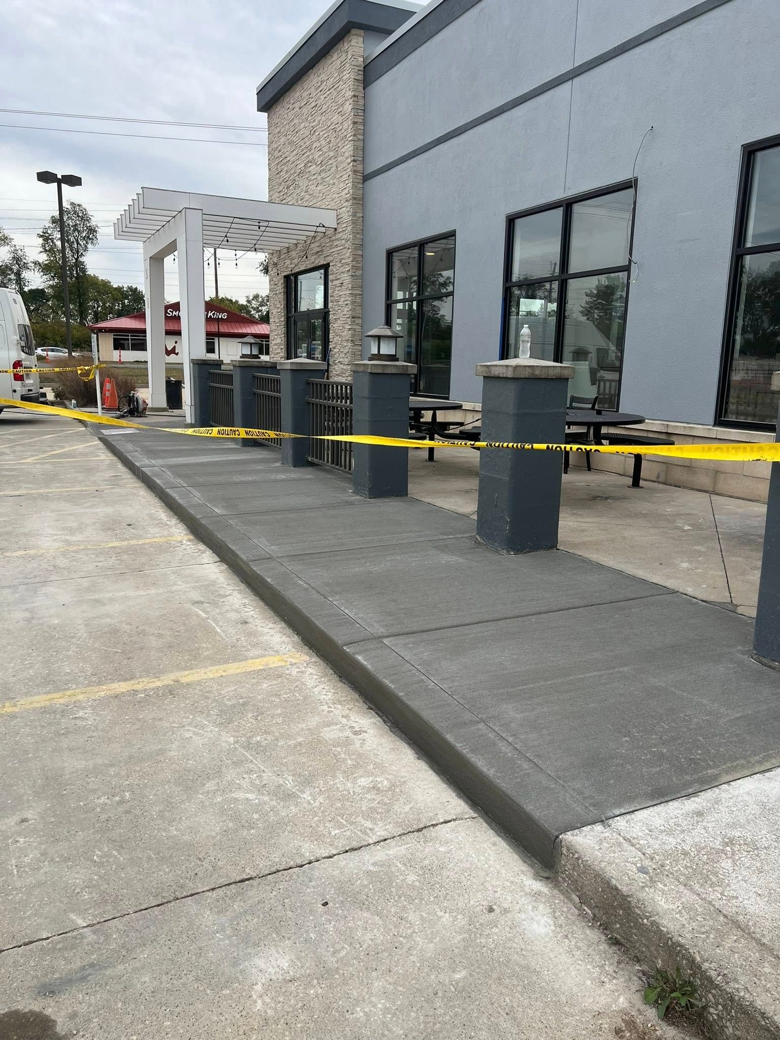 Exterior view of a building with a newly constructed concrete walkway and gray pillars; yellow caution tape is present.