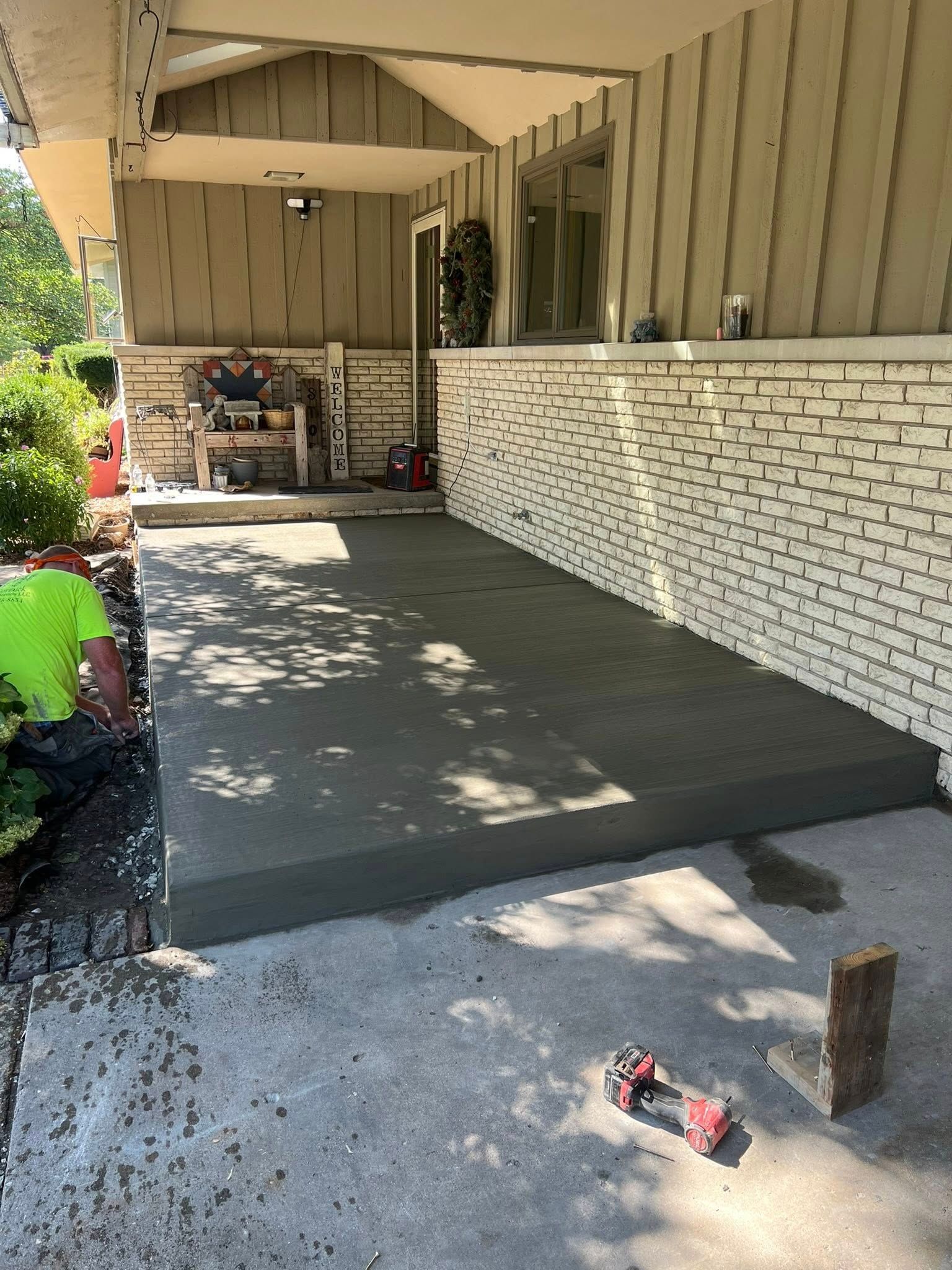 Newly poured concrete porch with a worker on the left. White brick wall and beige siding overhead.