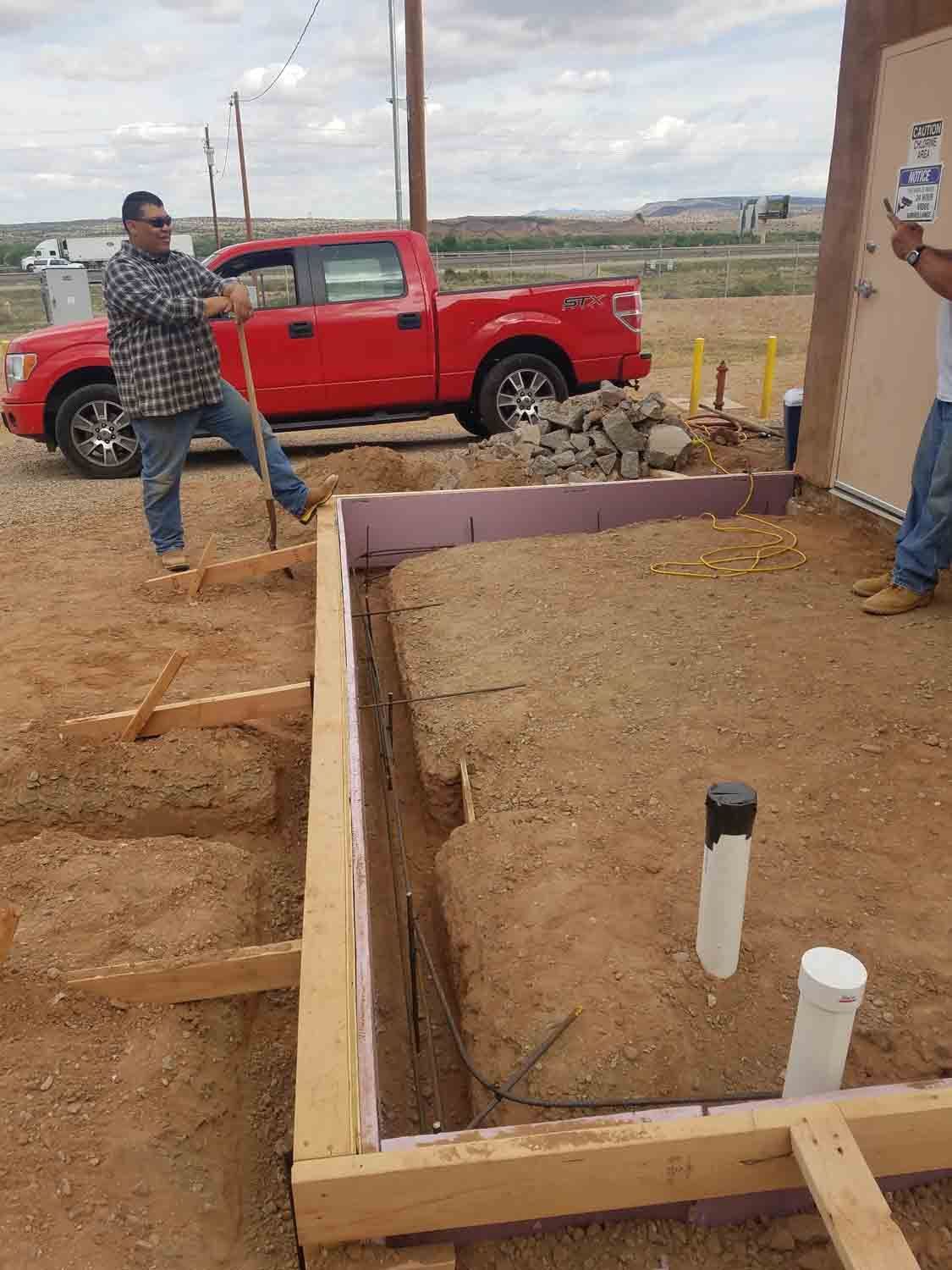 A man is digging a hole in the dirt next to a red truck.