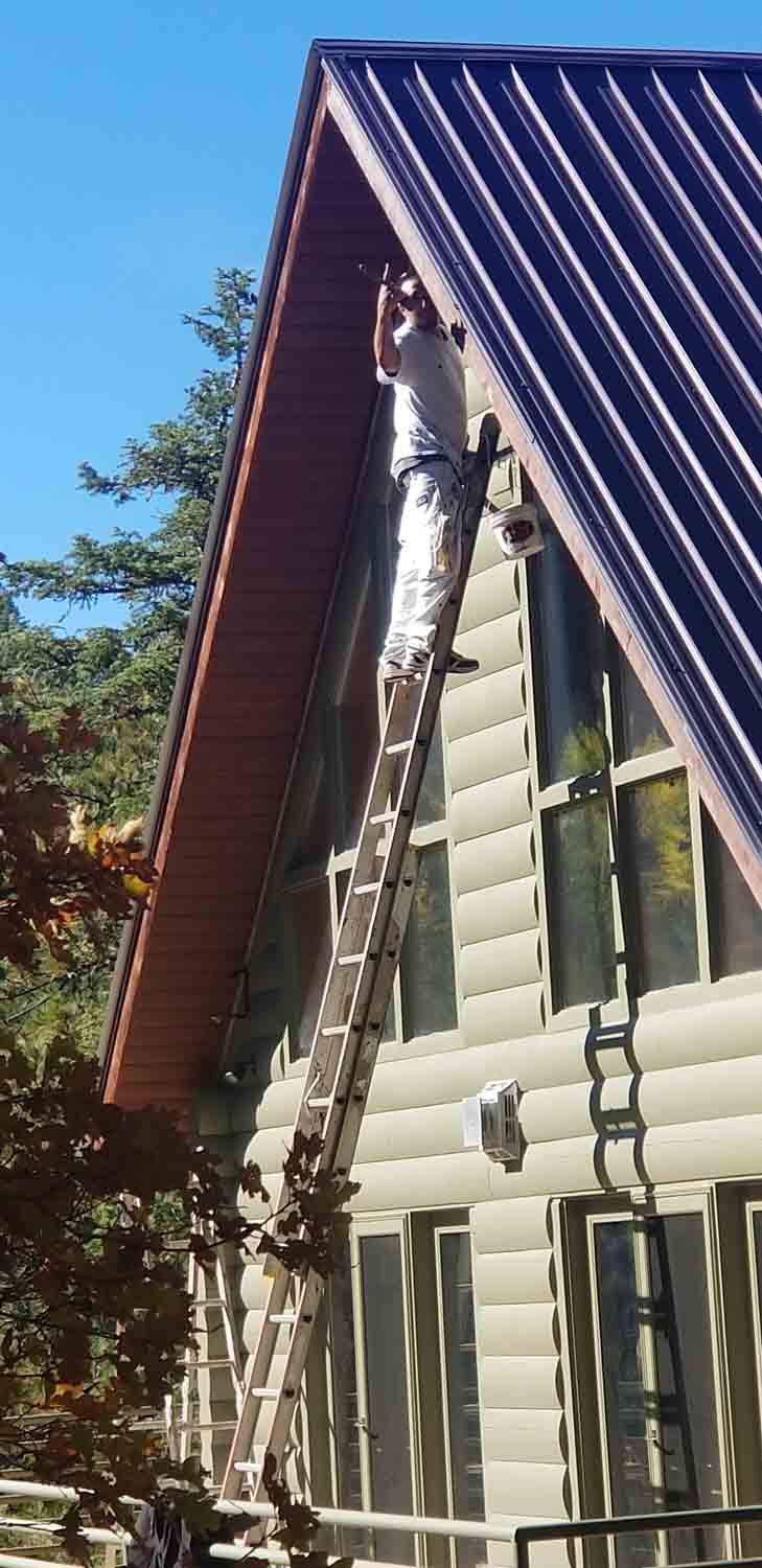 A man is standing on a ladder on the side of a house.