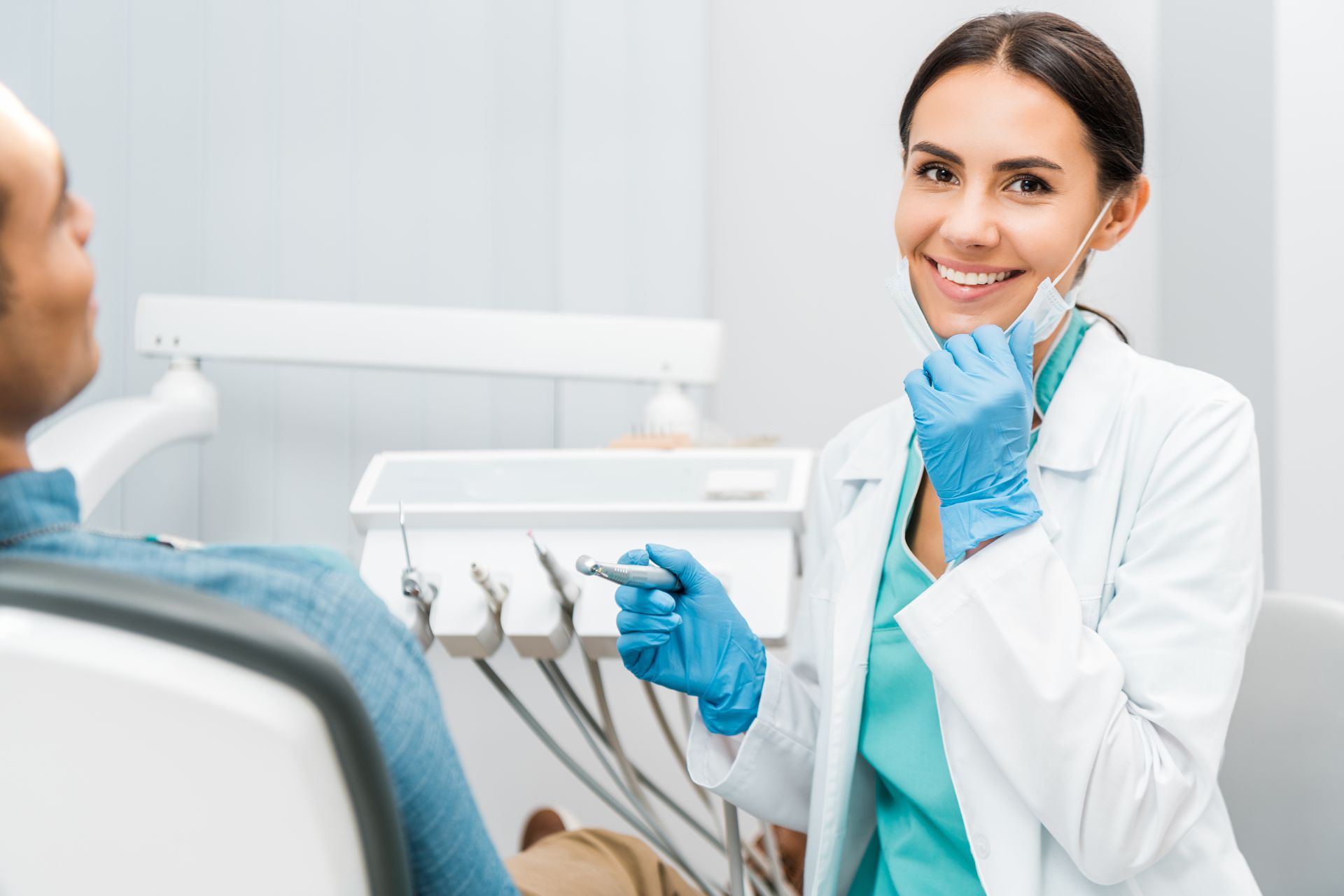 Dentist smiling warmly, patient seated in chair, tools visible in clinic.