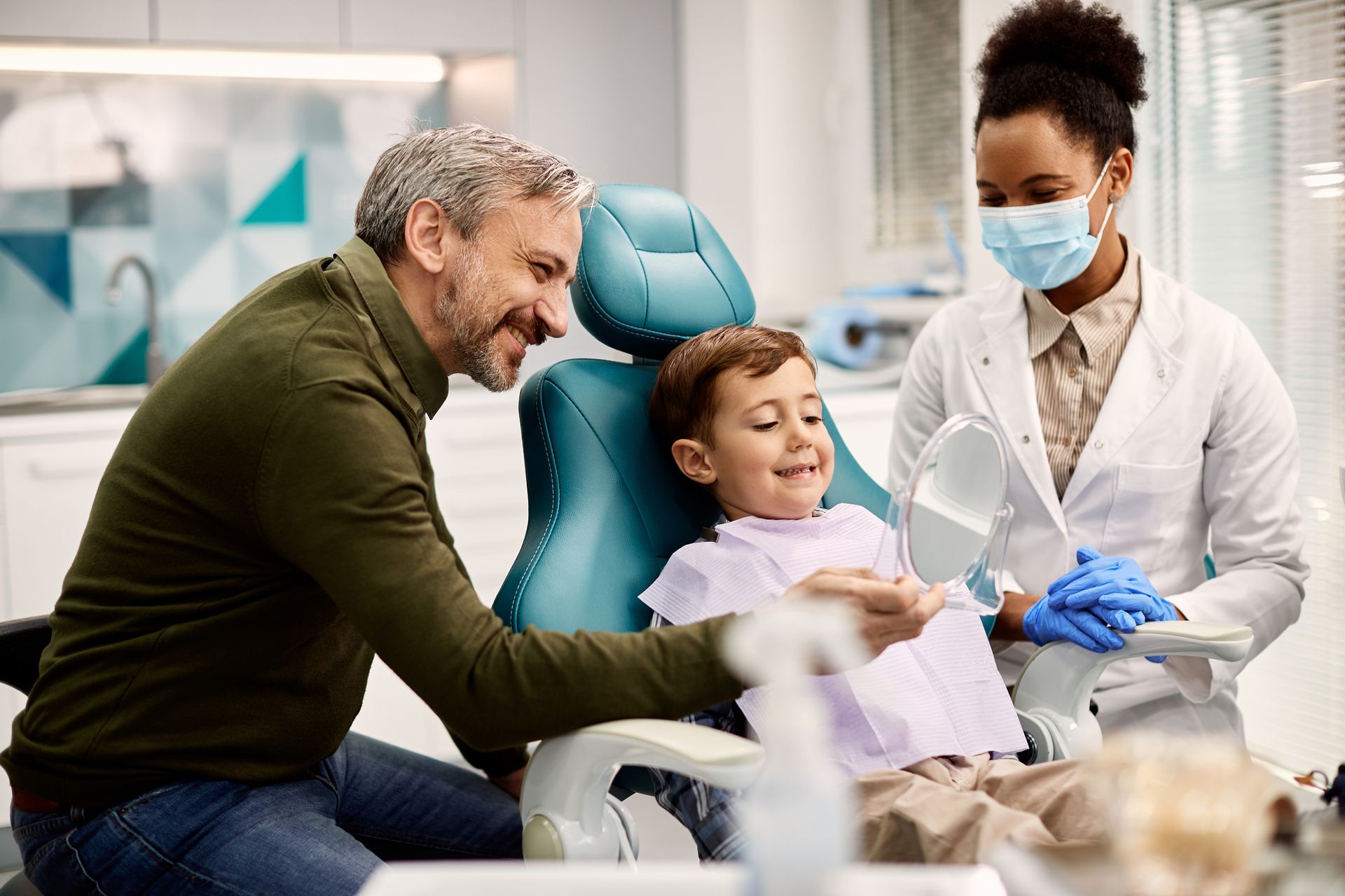 Child in dental chair with dentist and adult.