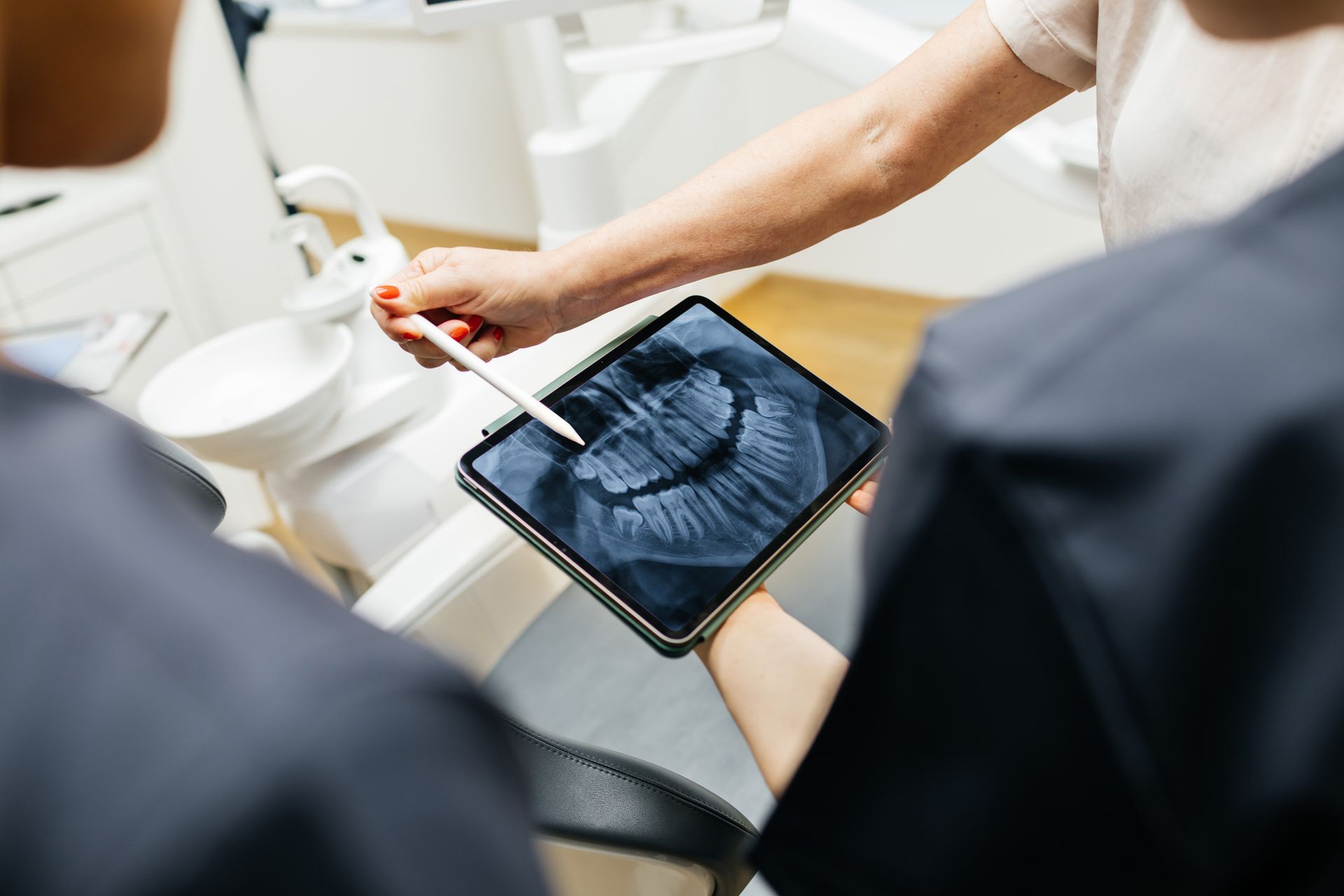 Dental professional shows X-ray on tablet while discussing teeth with patient.