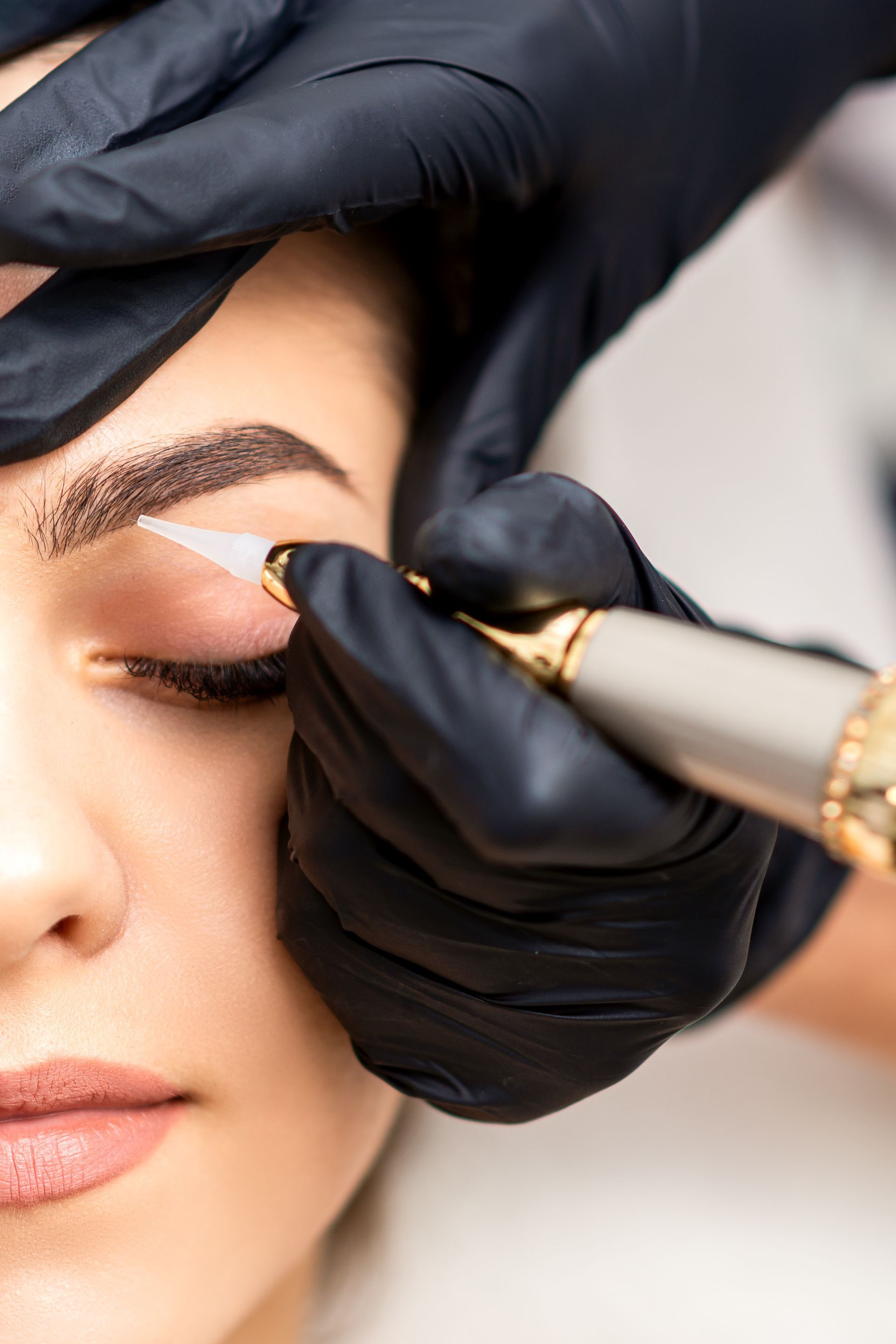 a woman has her eyebrows tattooed by a person wearing black gloves