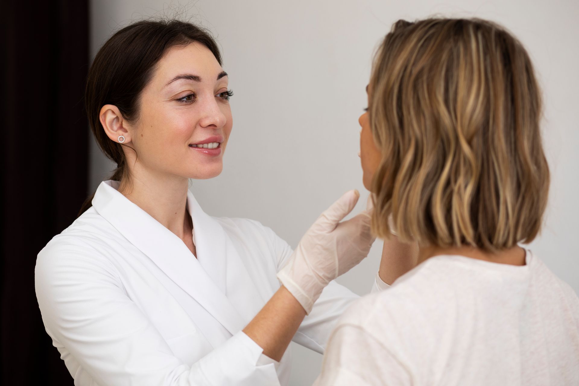 a woman in a white coat is examining another woman 's face
