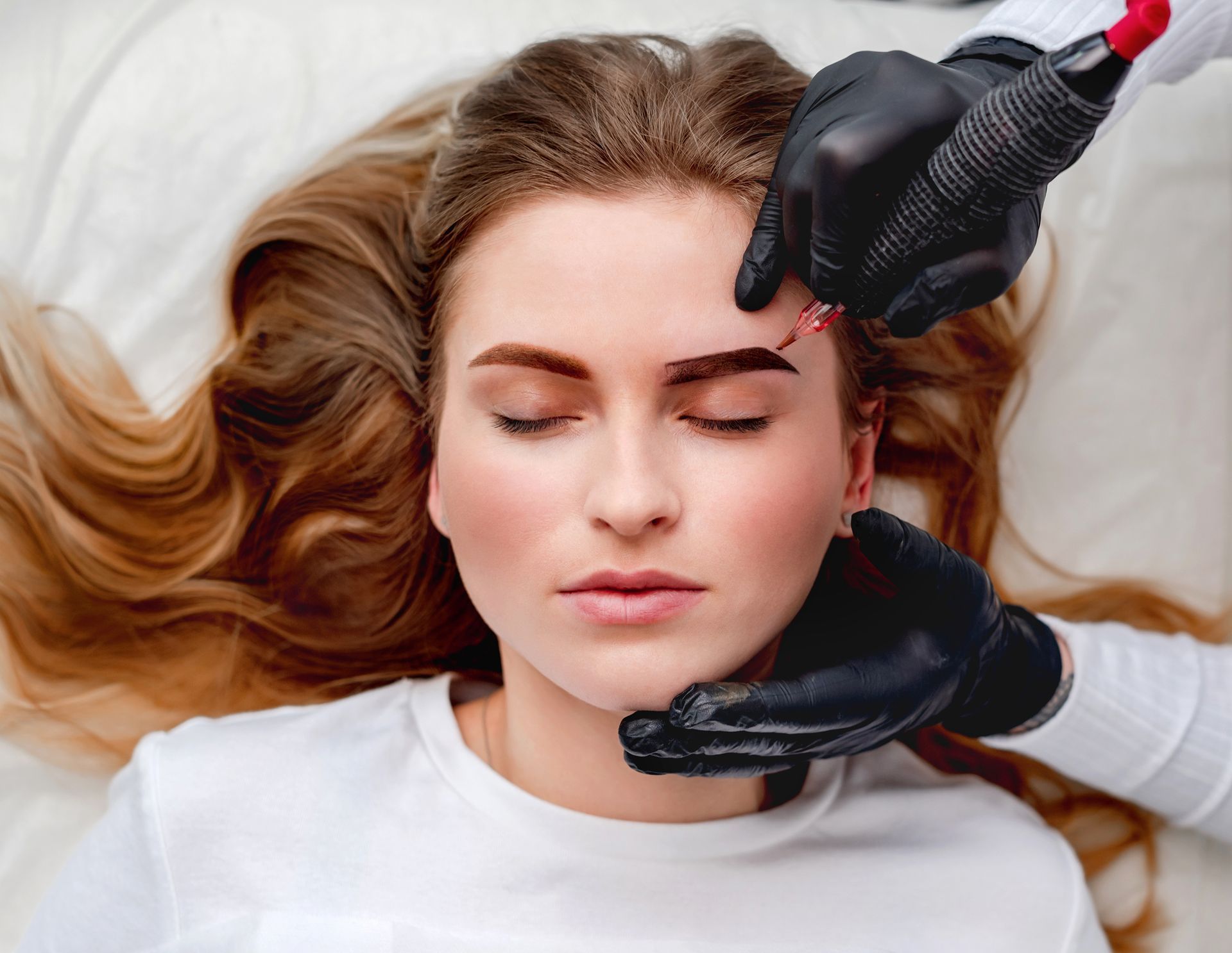 a woman is getting her eyebrows tattooed by a person wearing black gloves