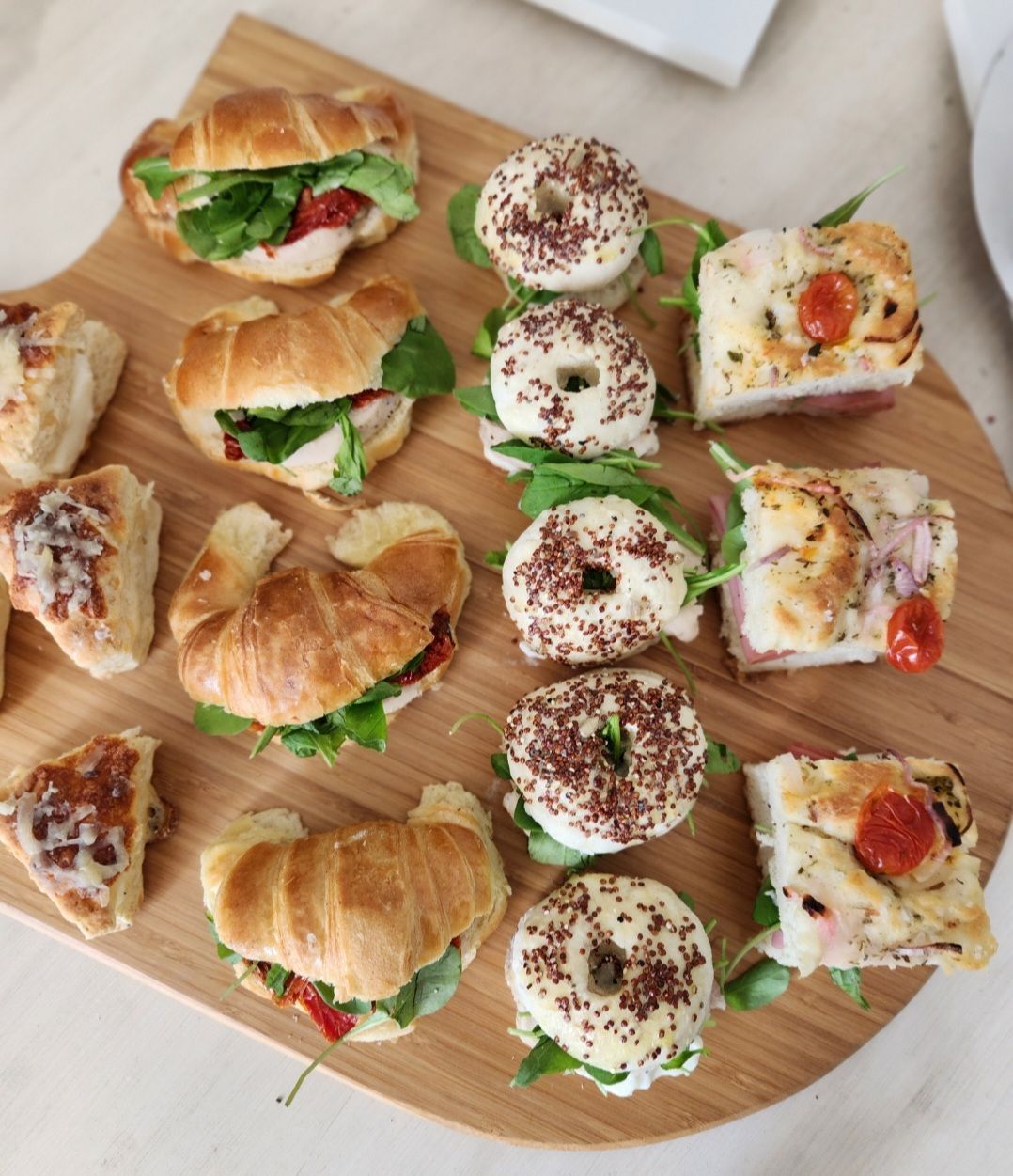 Una tabla de cortar de madera cubierta con una variedad de sándwiches y donas.