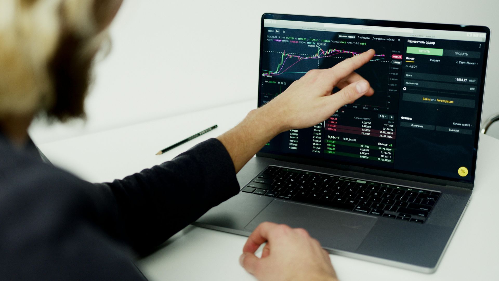 Person points at a laptop screen displaying stock charts, likely analyzing the market.