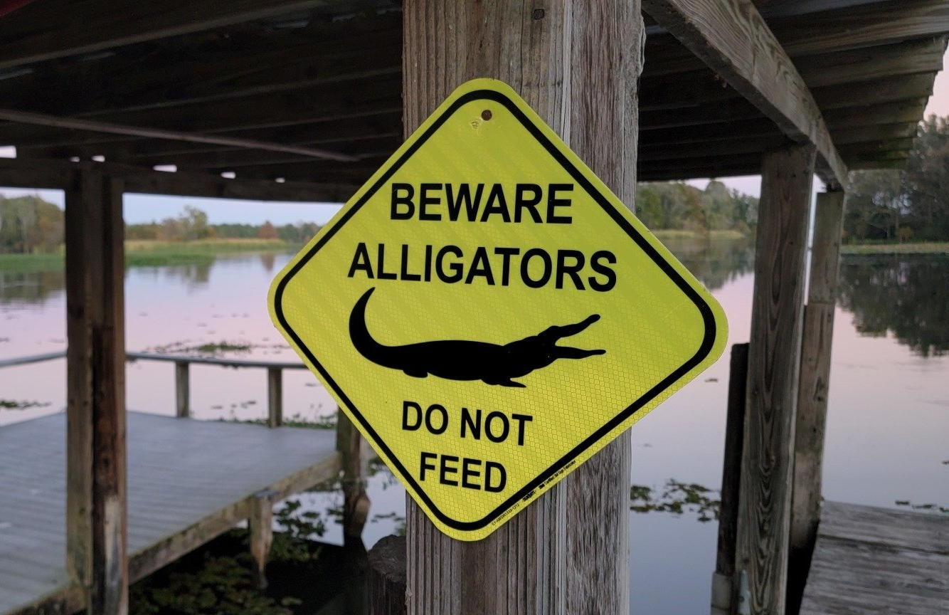 Beware alligators sign on dock post with lake in background