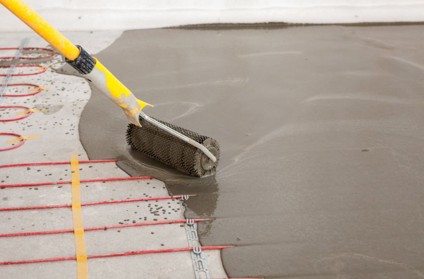 A Person is Spreading Concrete on a Floor With a Roller — HJK Plastering In Byron Bay, NSW