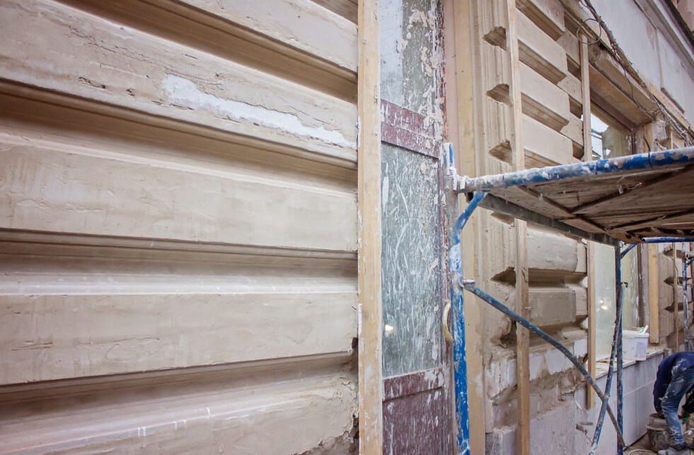 A Man is Standing on a Scaffolding Next to a Wooden Wall — HJK Plastering In Byron Bay, NSW