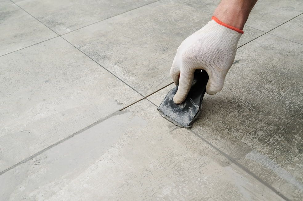 A Person is Applying Grout to a Tile Floor — HJK Plastering In Kyogle, NSW