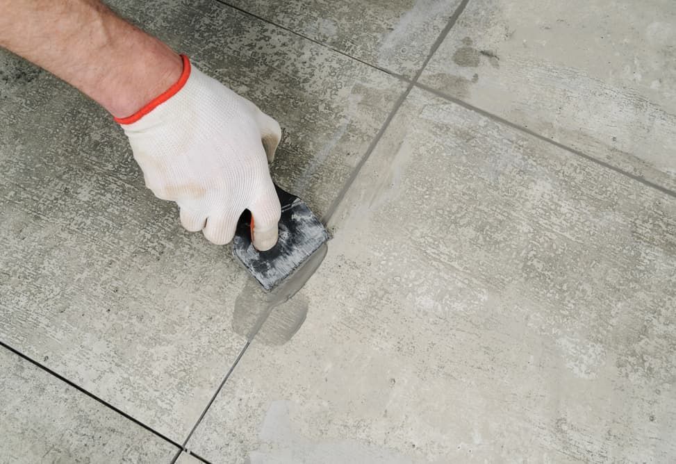 A Person is Using a Spatula to Repair a Tile Floor — HJK Plastering In Northern Rivers, NSW