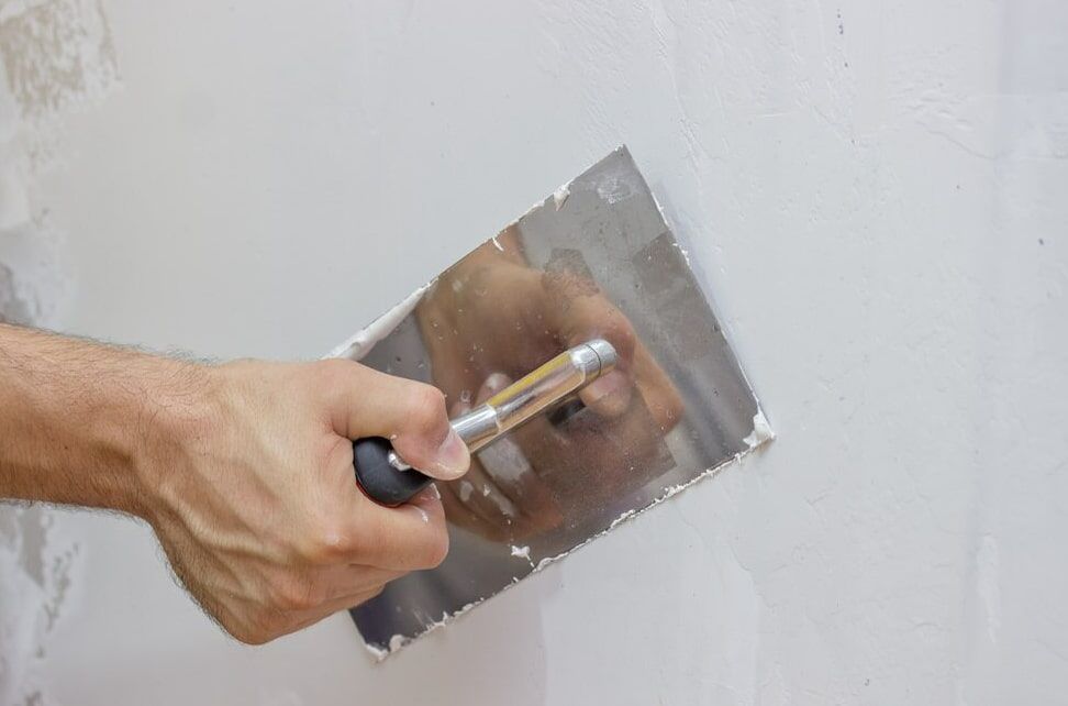A Man is Plastering a Wall With a Trowel — HJK Plastering In Byron Bay, NSW