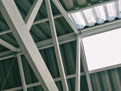 Green metal roof structure with white support beams and a bright skylight panel