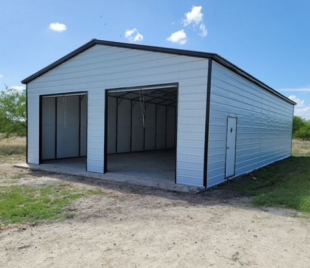 Metal-sided barn-style shed with open front bays on a dirt lot under a blue sky