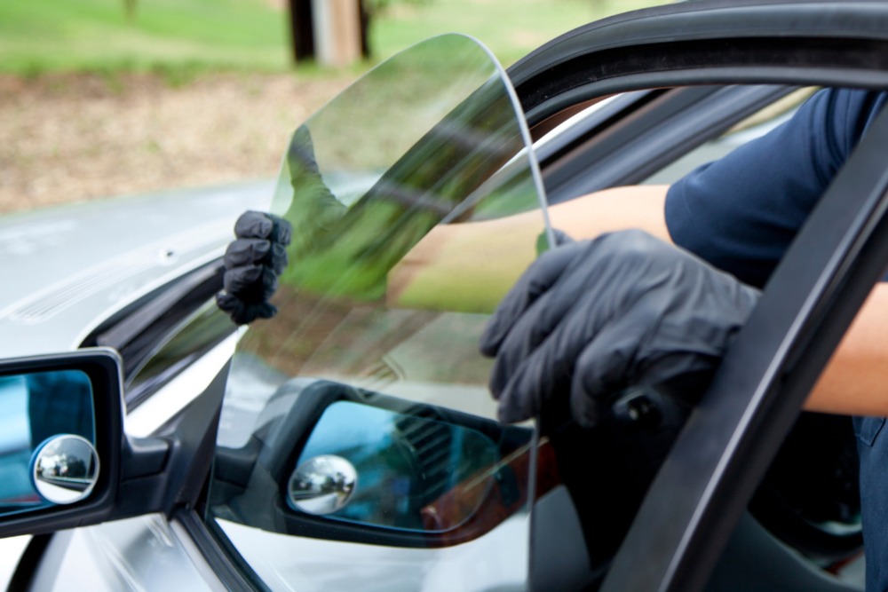 Gloved hands removing a car windshield tint film on a black vehicle