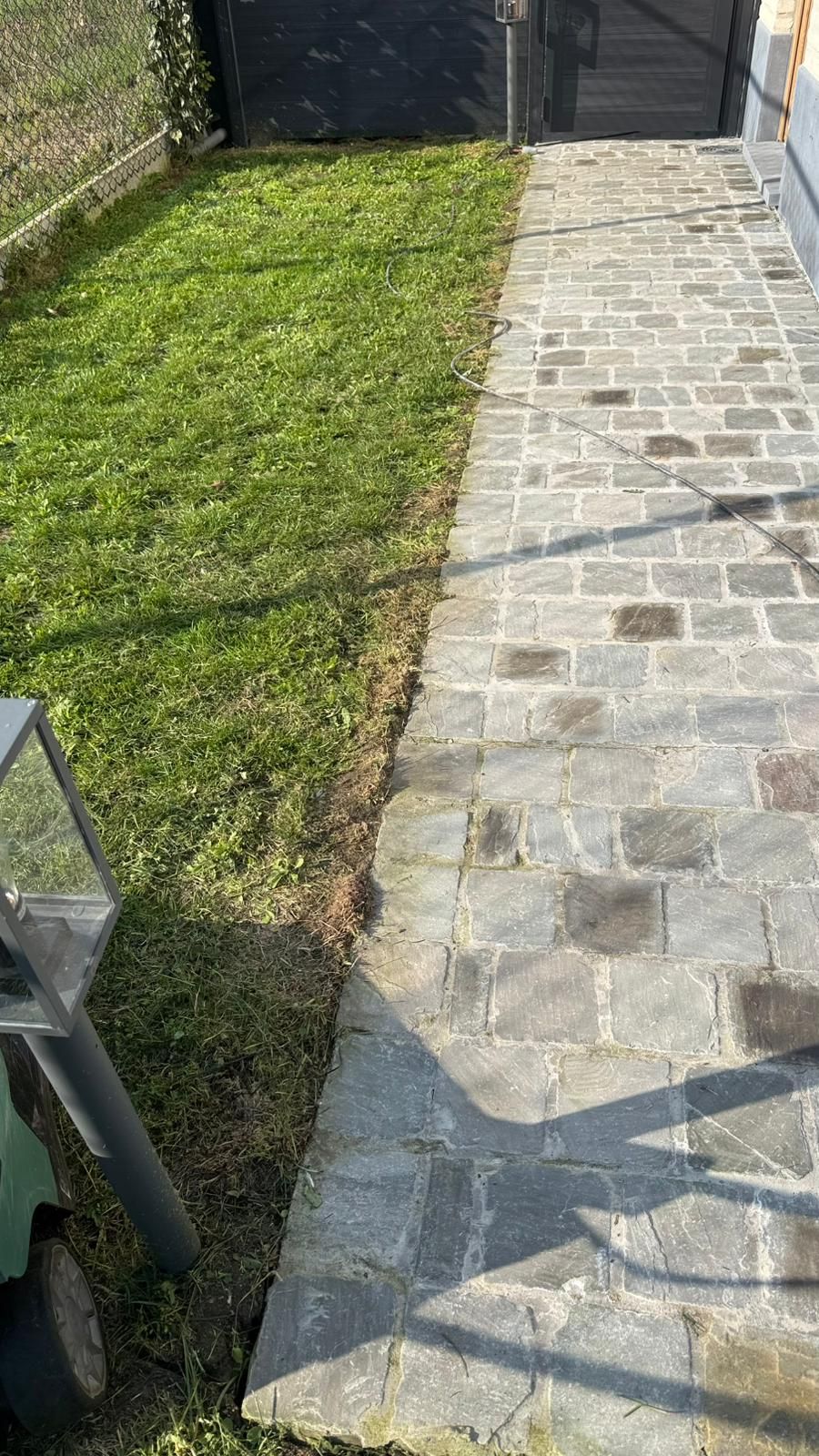 Een geplaveid pad loopt langs een stukje groen gras in een zonnige buitenomgeving.