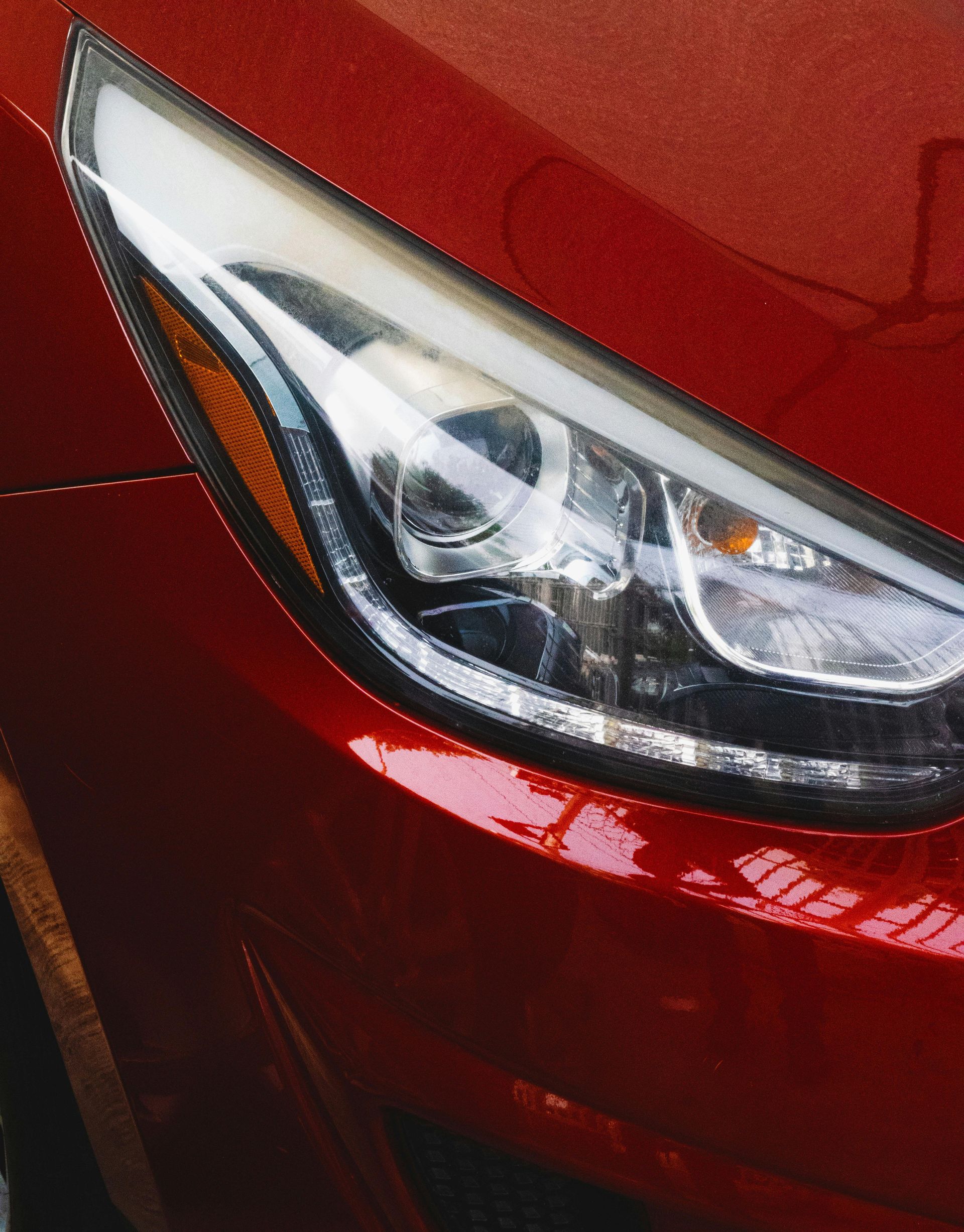 Een close-up van een strakke, moderne autokoplamp op een glanzende rode carrosserie.
