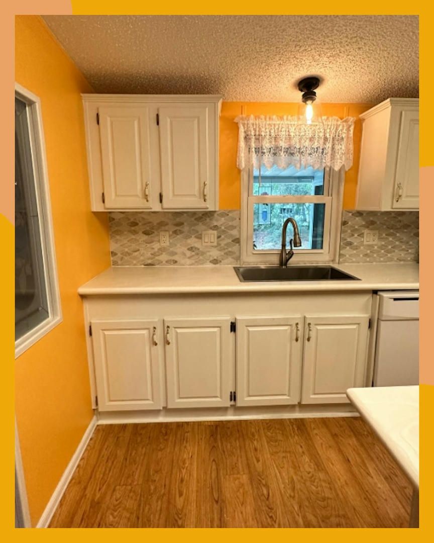 Kitchen with white cabinets, light countertops, and orange walls; window with sink and faucet.