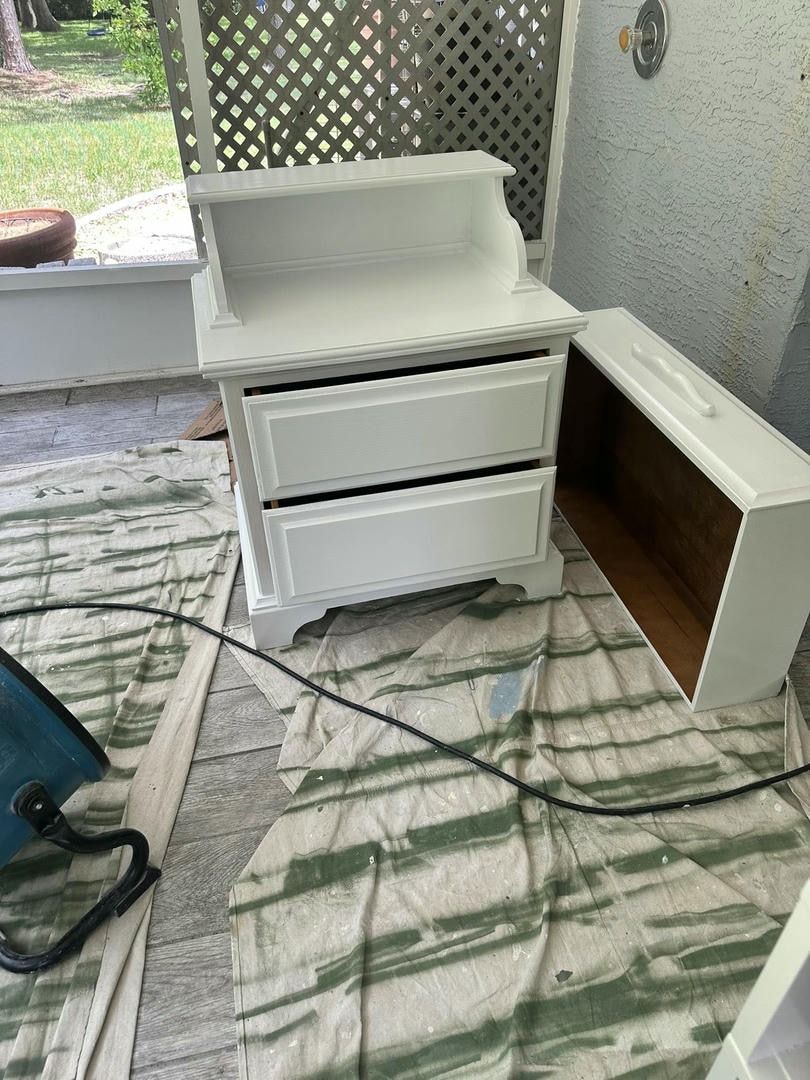 White painted nightstand with two drawers and an open drawer on a paint splattered cloth.