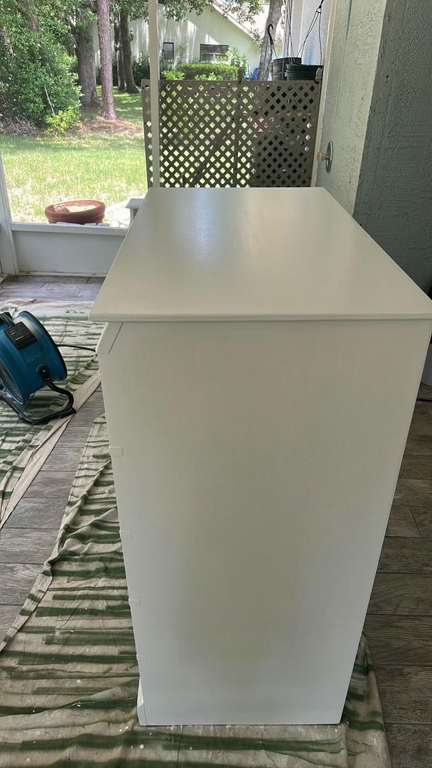 White painted cabinet on green drop cloth, outdoors. A teal saw is to the side.