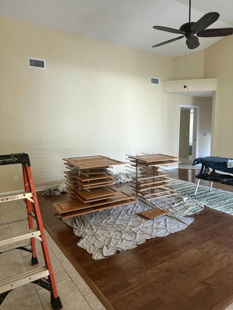 Room interior with wooden cabinet doors stacked on a large table, a ladder, and ceiling fan.