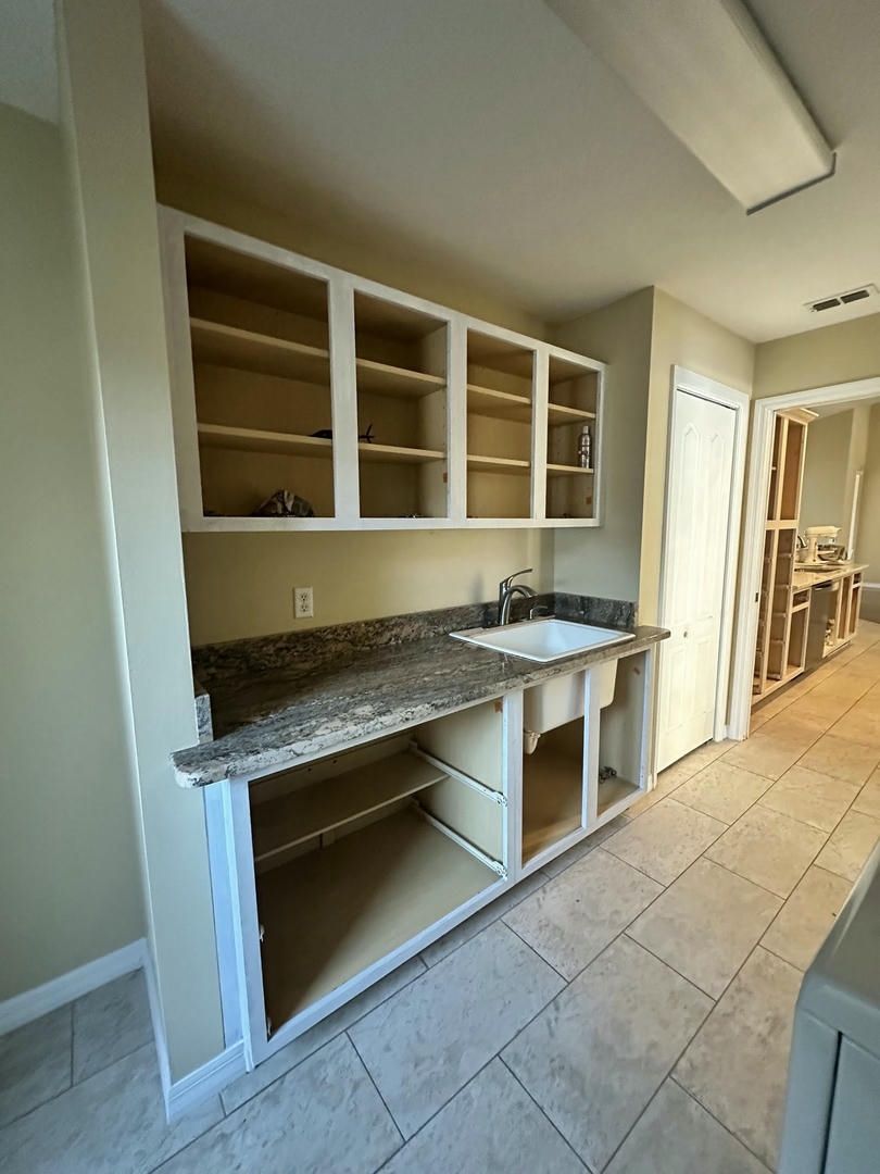 Kitchen cabinets with sink and granite countertop, under construction; beige walls and tile floor.