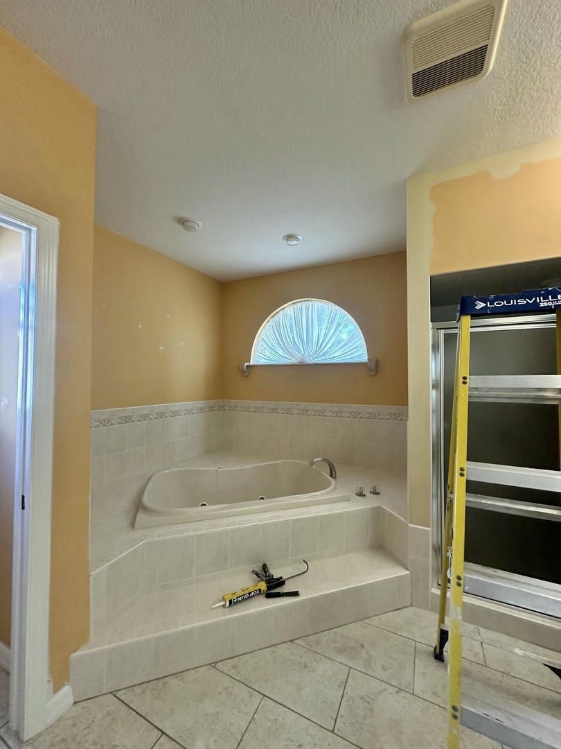Bathroom with built-in tub on a tiled platform. A ladder stands next to a shower. Peach walls.