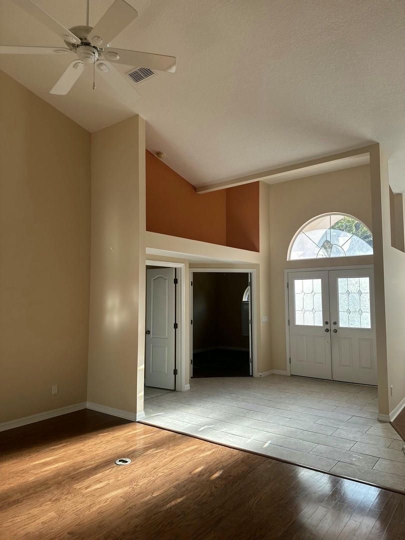 Spacious room with high ceilings, arched windows, and a doorway. Hardwood and carpeted flooring.