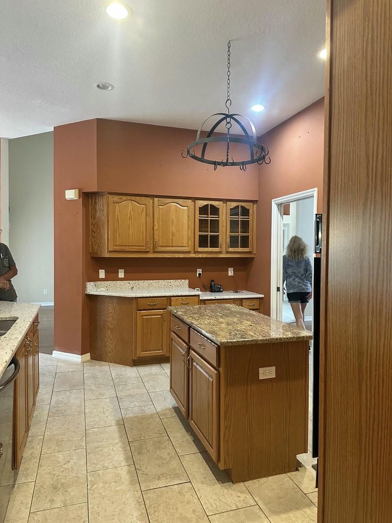 Kitchen with island, wood cabinets, stone countertops, and a person walking through a doorway.