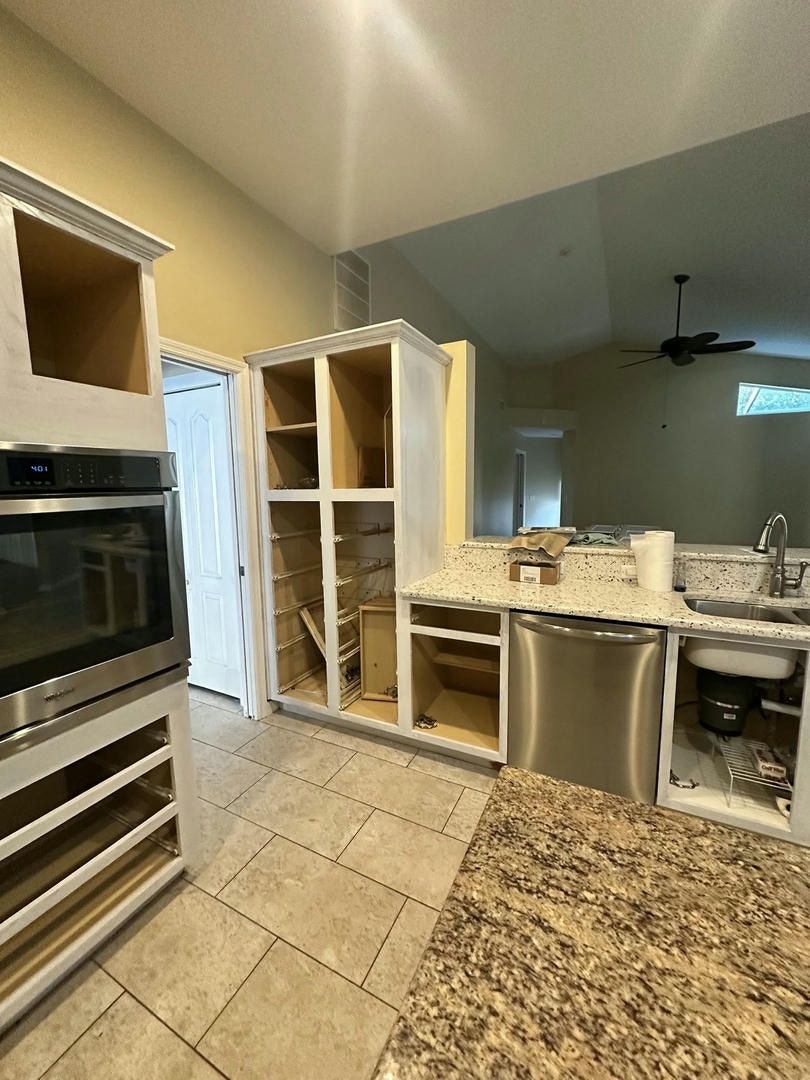 Kitchen remodel in progress: unfinished cabinets, oven, and dishwasher; beige walls; open view to living area.