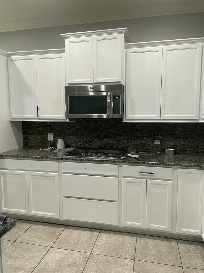 White kitchen cabinets with granite countertop, stainless steel microwave, and backsplash.