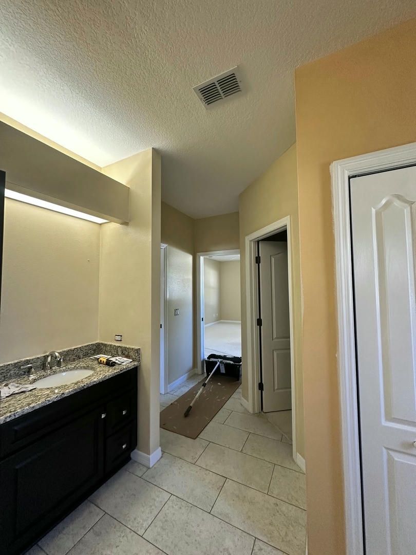 Bathroom hallway with vanity, closed door, and hallway leading to a bedroom. Yellow and cream walls.