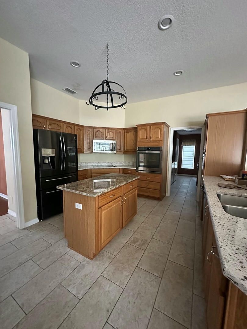 Kitchen with wooden cabinets, granite countertops, tile floor, and a black refrigerator.