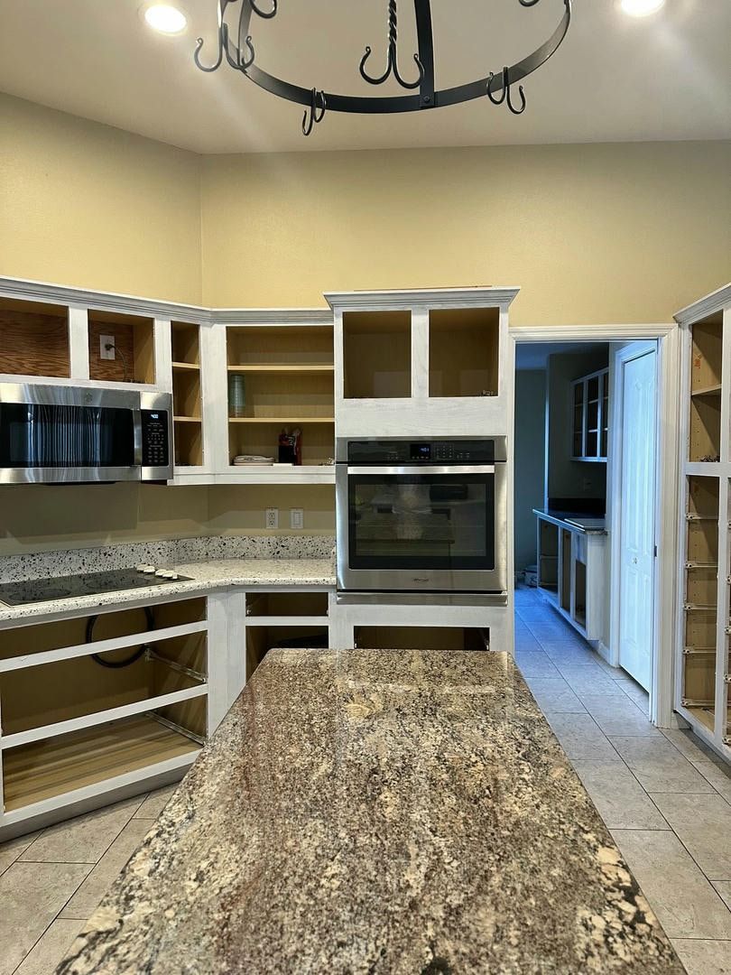 Kitchen undergoing renovation with empty white cabinets, a granite countertop, and island.