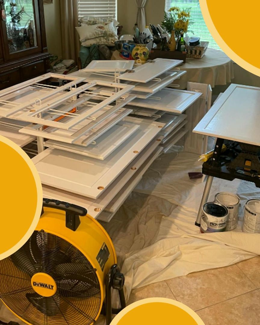 White cabinet doors stacked, drying indoors with a yellow fan and paint cans.
