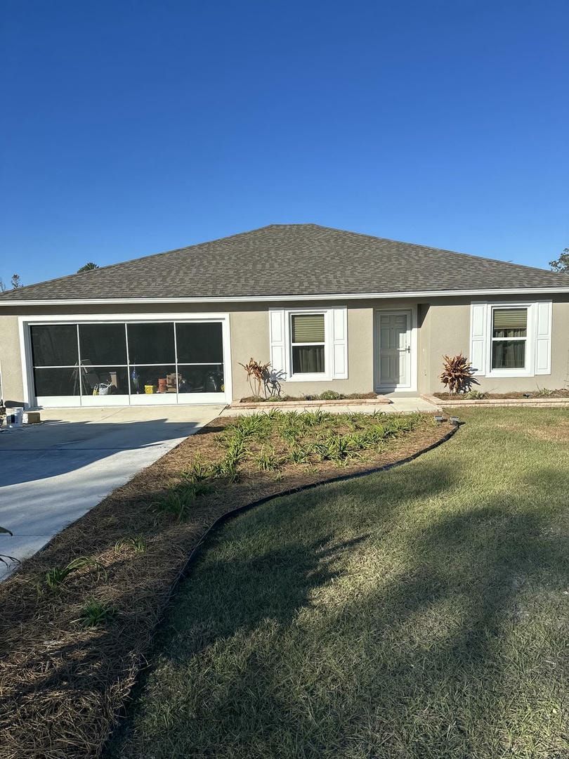 Tan stucco house with gray roof, small windows, and a screened-in garage. Blue sky.