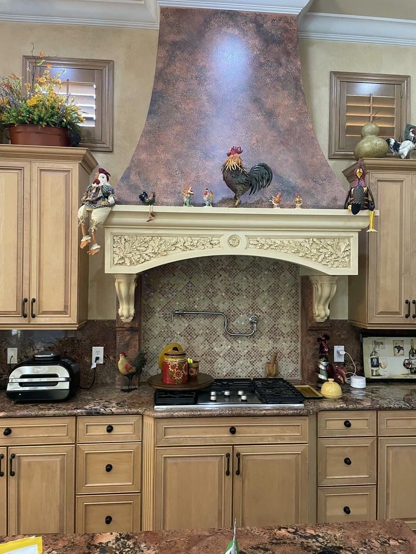 Kitchen with stove, cabinets, rooster decor, and ornate range hood.