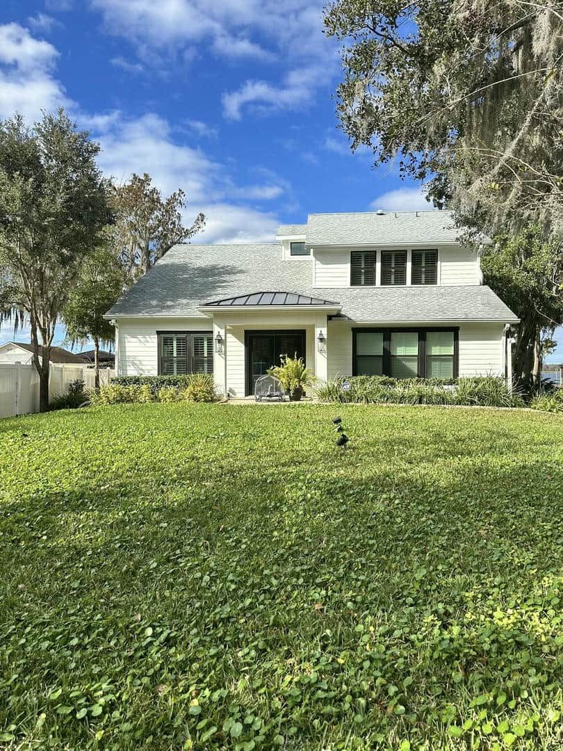 White house with black-trimmed windows, a dark front door, and a green lawn under a blue sky.